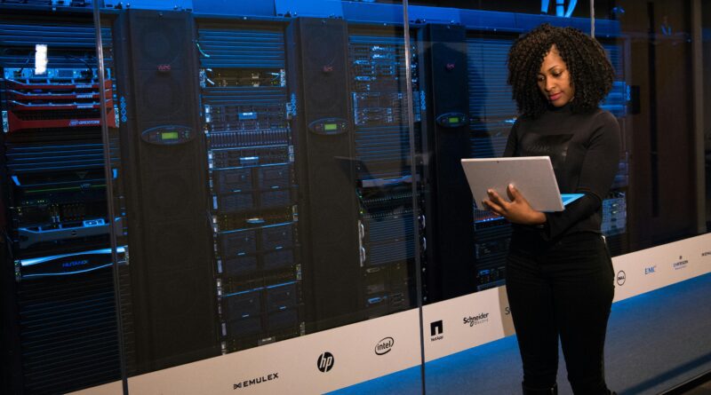 A female engineer using a laptop while monitoring data servers in a modern server room.