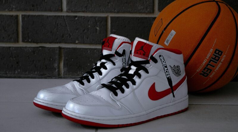 White and red basketball sneakers with an orange basketball on tiled floor.