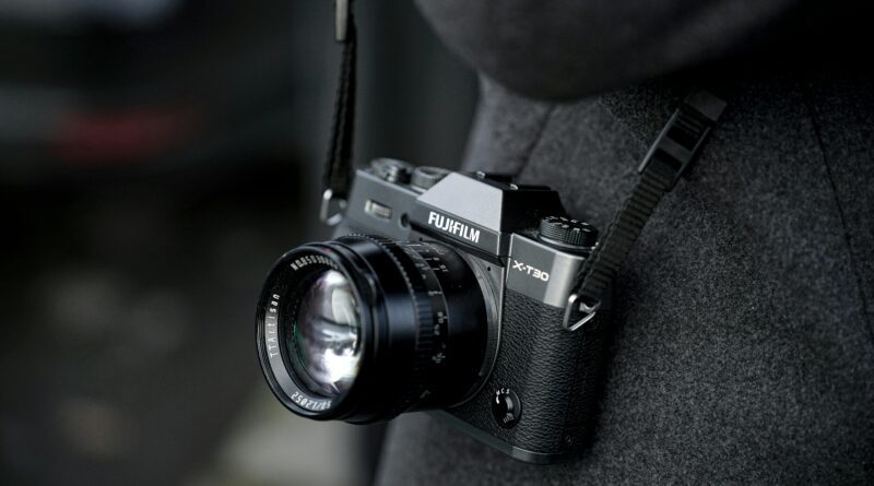 Detailed shot of a Fujifilm X-T30 camera hanging from a person's neck in a grey coat.