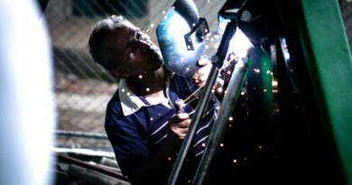 A professional welder working indoors, using safety equipment and producing bright sparks.