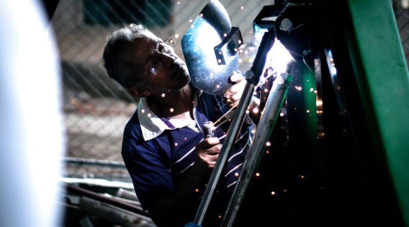 A professional welder working indoors, using safety equipment and producing bright sparks.